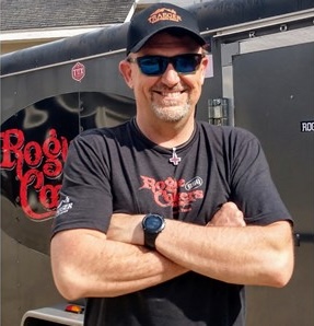 Doug Sheiding standing arms folded, sunglasses on.