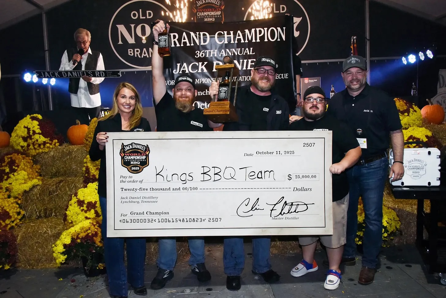 The Grand Champion of the Jack Daniel's World Championship Invitational Barbecue holding the winner's check and hoisting a bottle of Jack Daniel's whiskey.