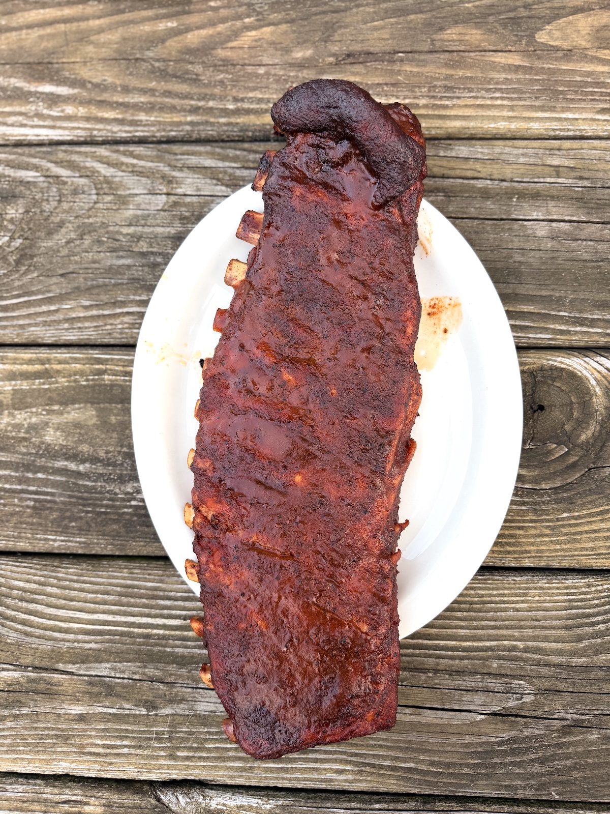 Rack of smoked ribs on a white plate on a wooden picnic table.
