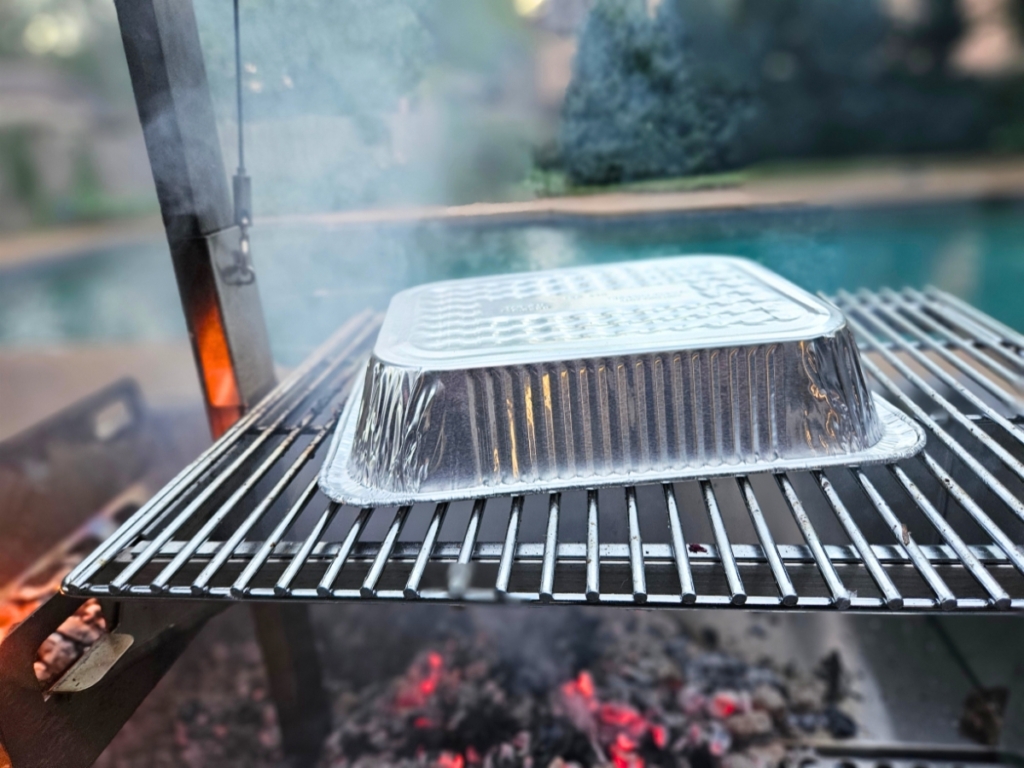 Inverted aluminum half pan on a grill grate.