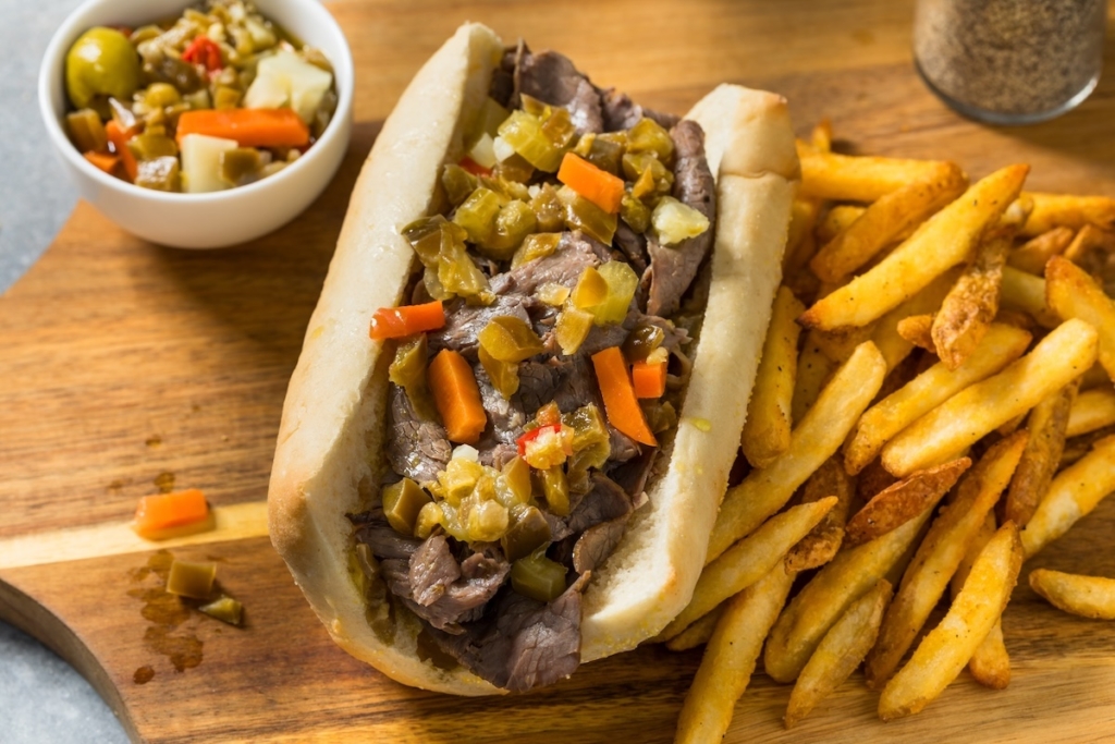 Homemade Chicago Italian beef sandwich with giardiniera on a cutting board with French fries nearby.