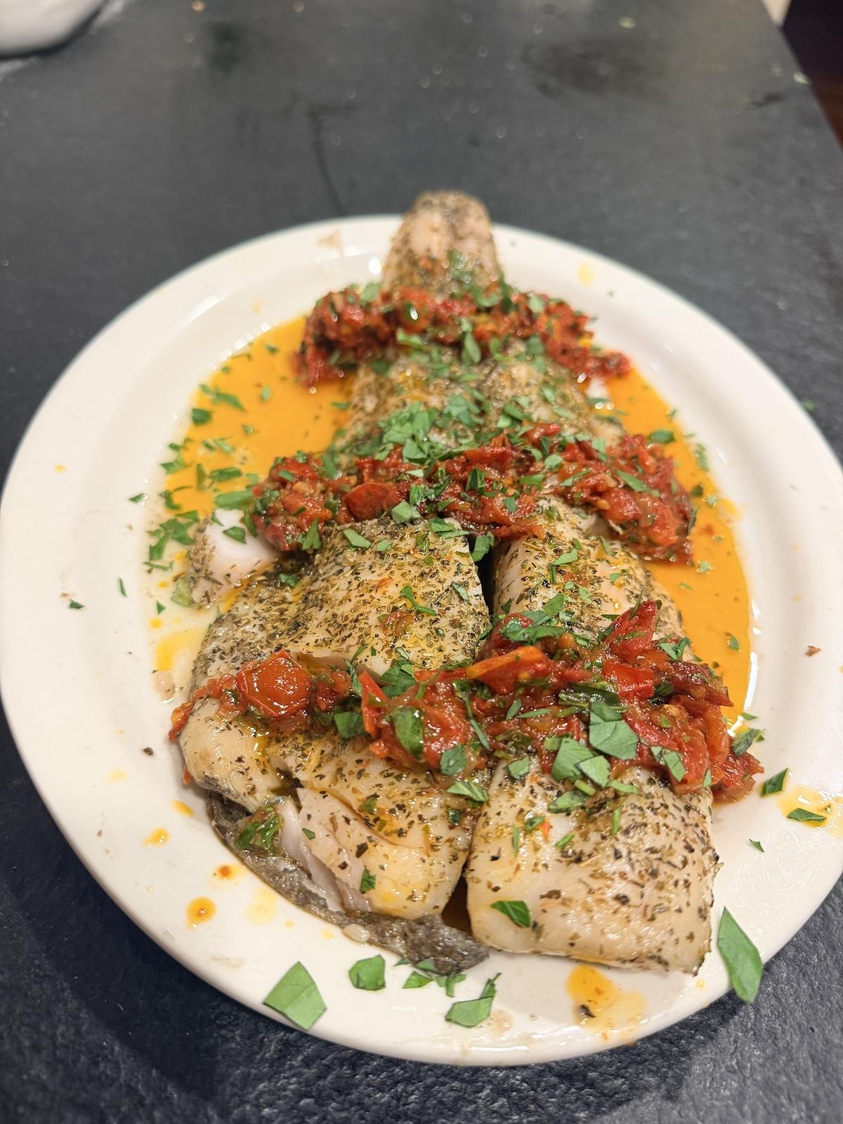 Grilled black cod (sablefish) shown on a plate with tomato sauce and herbs.