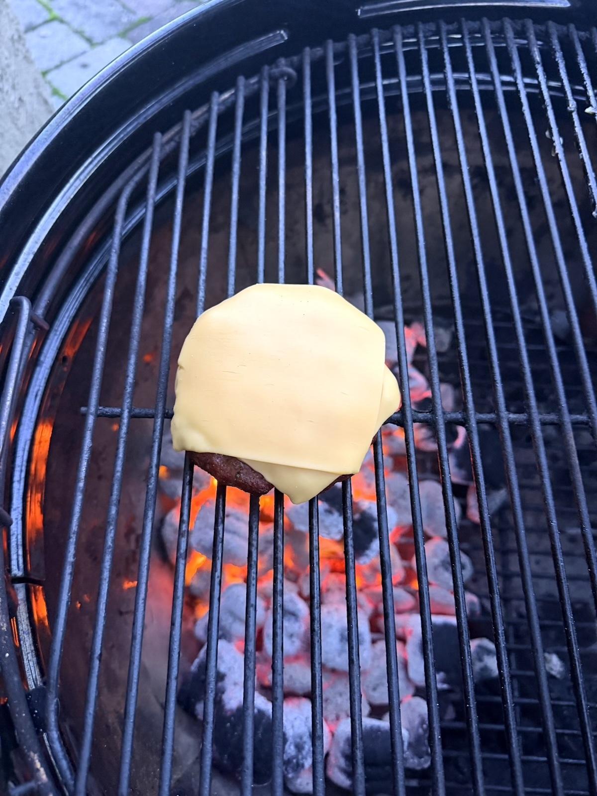 Cheeseburger cooking on a charcoal grill with Weber Kettle Smart Ring installed.